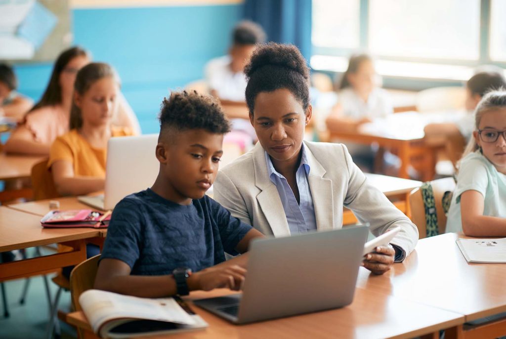 teacher and her student using laptop during computer class