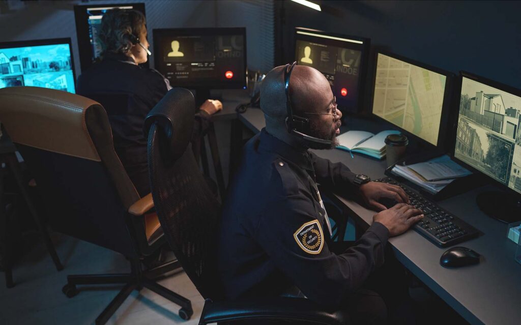 law enforcement officers wearing headset monitoring security footage on multiple computer screens in control room